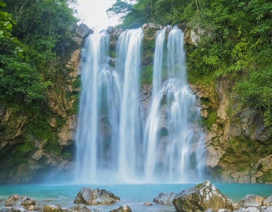 A cascading waterfall surrounded by lush greenery and clear turquoise water.